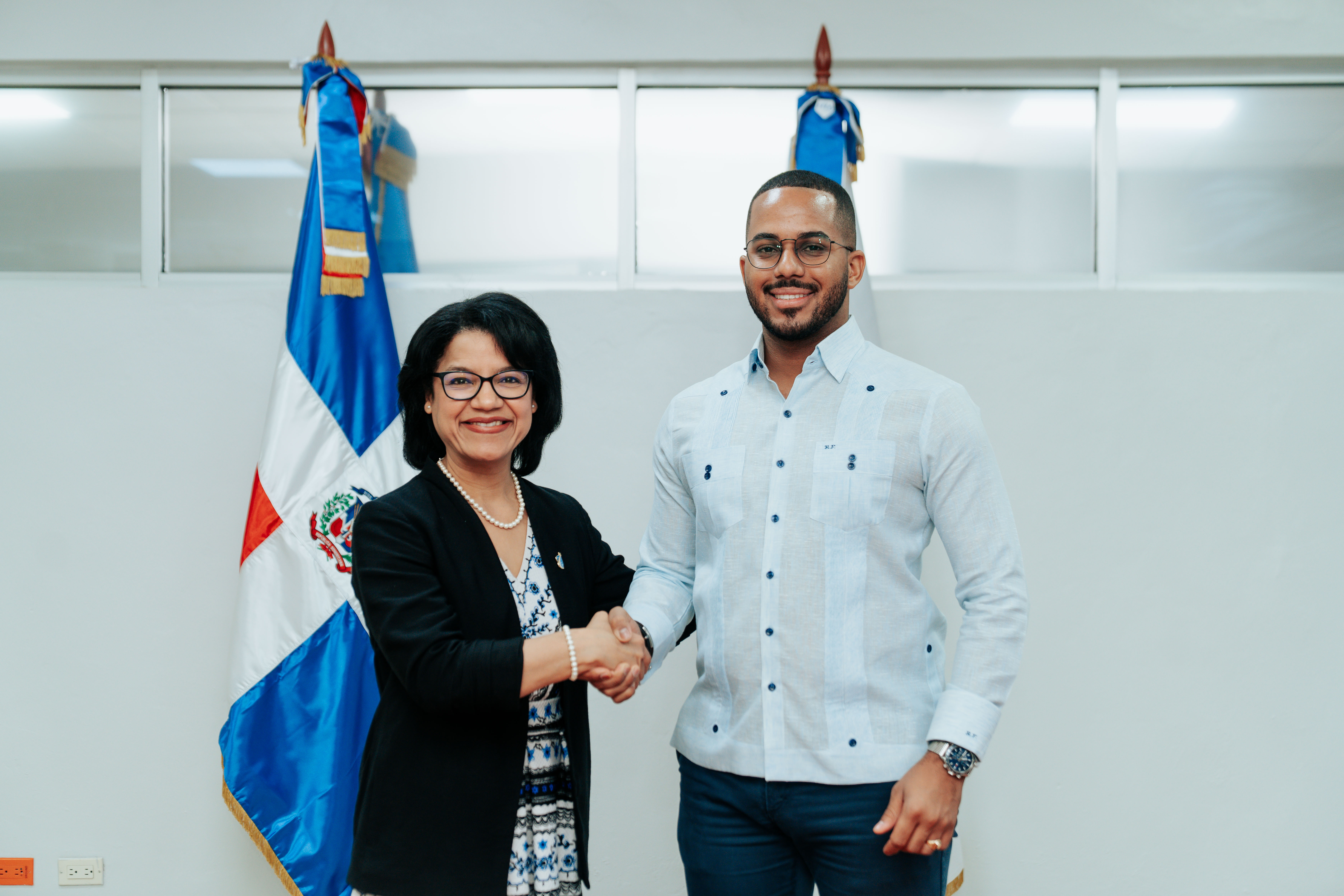 Formal handshake between NECC and ITLA representatives in front of Dominican Republic flags