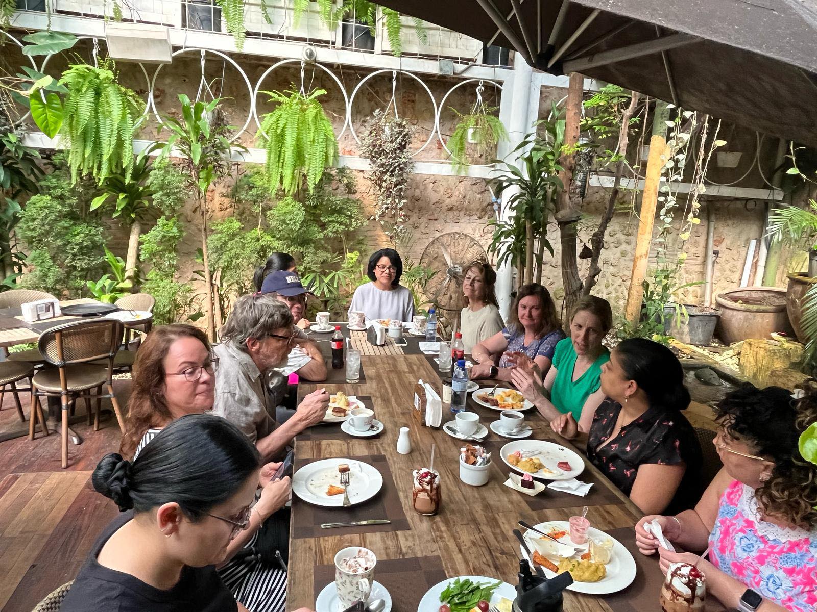 Delegation members gathered around wooden table for debrief breakfast in lush garden setting