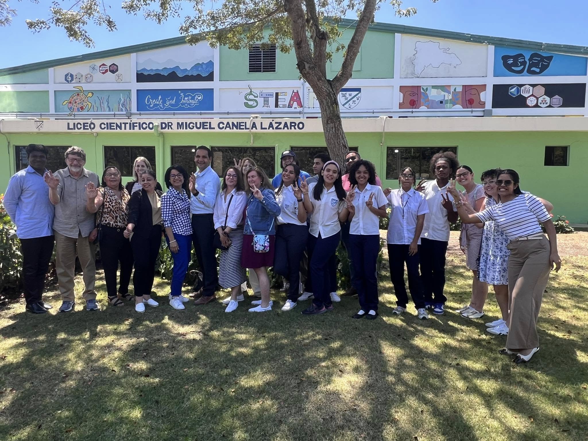 Group photo with students and staff in front of the green Liceo Científico building with STEM and arts murals