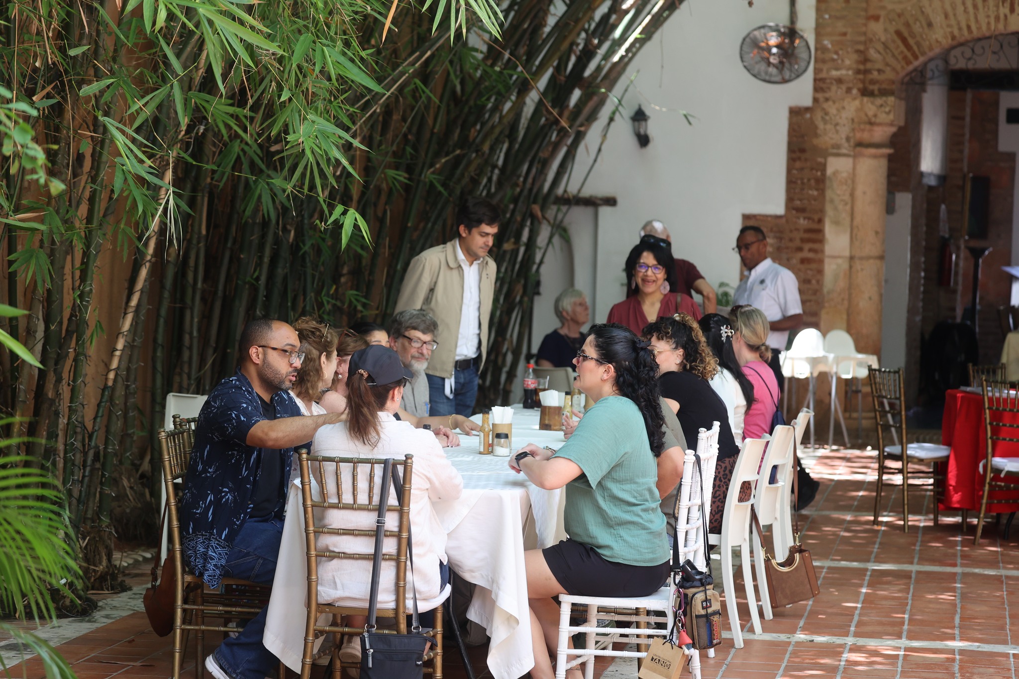 Delegation members seated at white-clothed tables with Oscar Polanco in elegant restaurant courtyard with bamboo backdrop