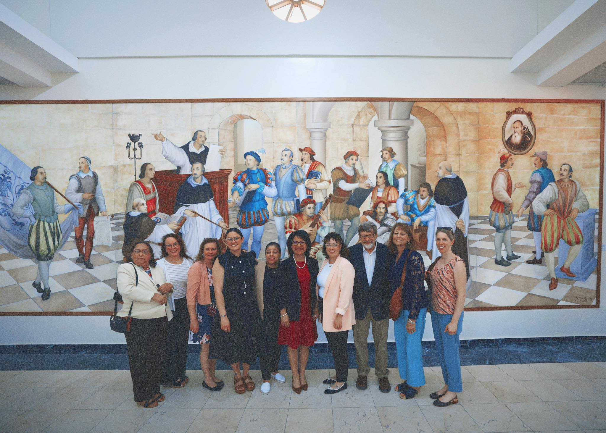 Group photo in front of a historical mural depicting the university's founding