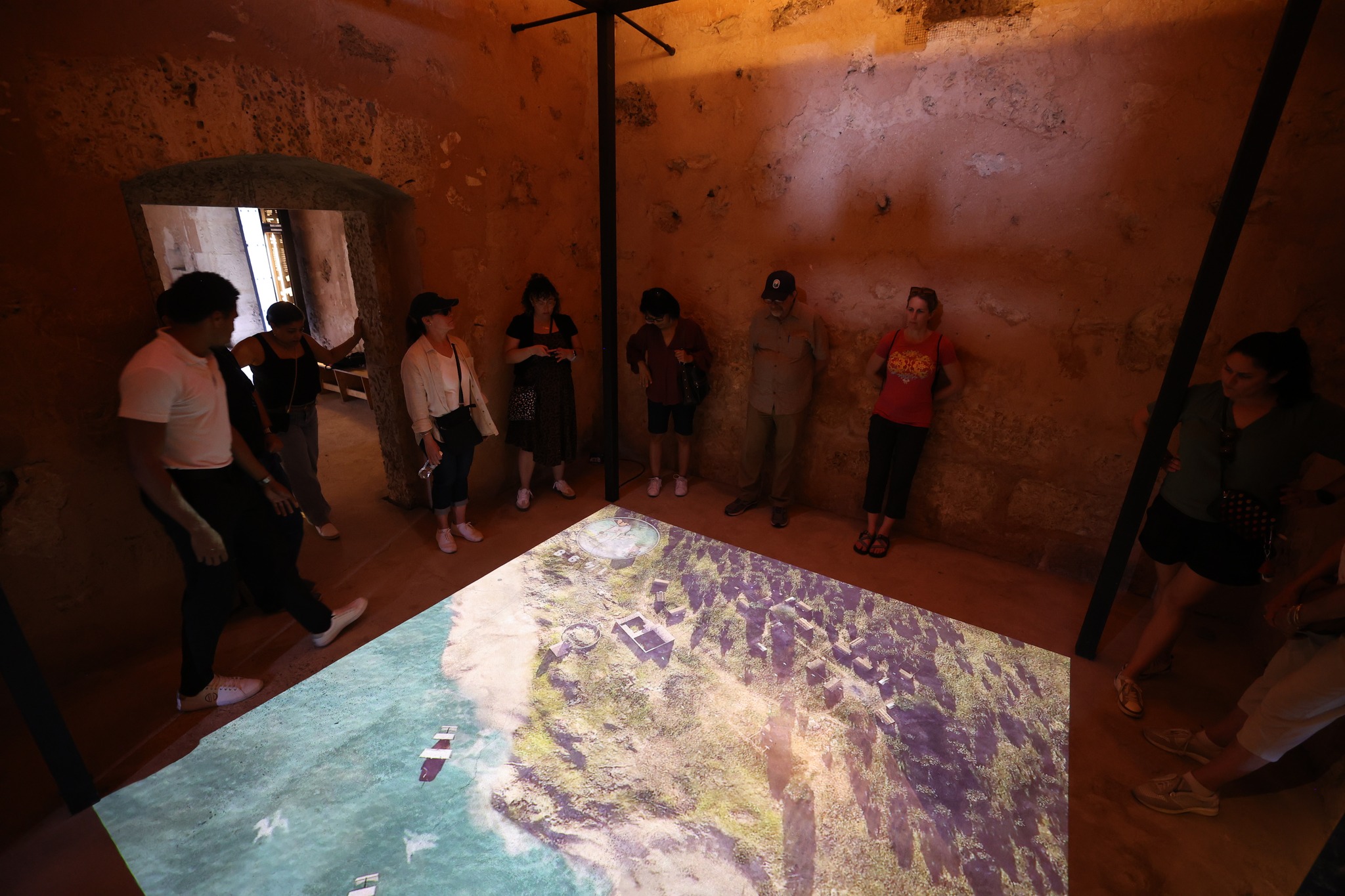 Floor projection showing aerial view of the coastal settlement in a dimly lit stone room