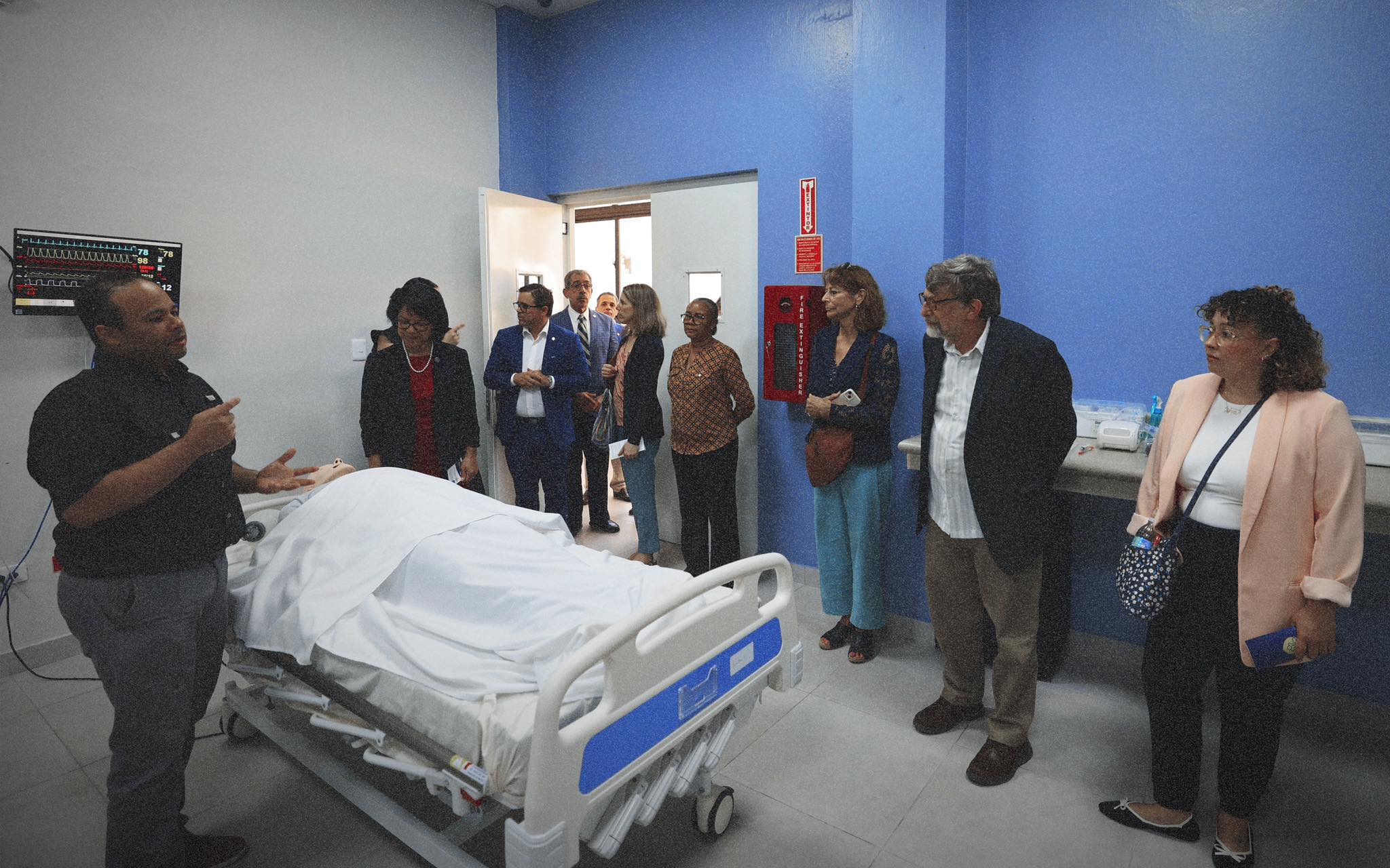 Medical instructor demonstrating hospital bed and monitoring equipment to visitors