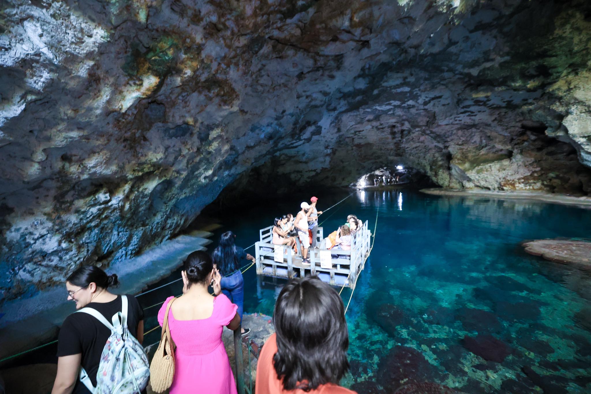 Group observing hand-pulled raft crossing luminous turquoise cave waters