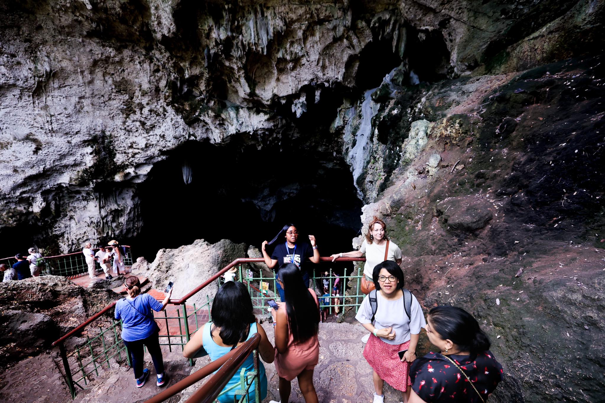 Group members descending stone steps at cave entrance with safety railings
